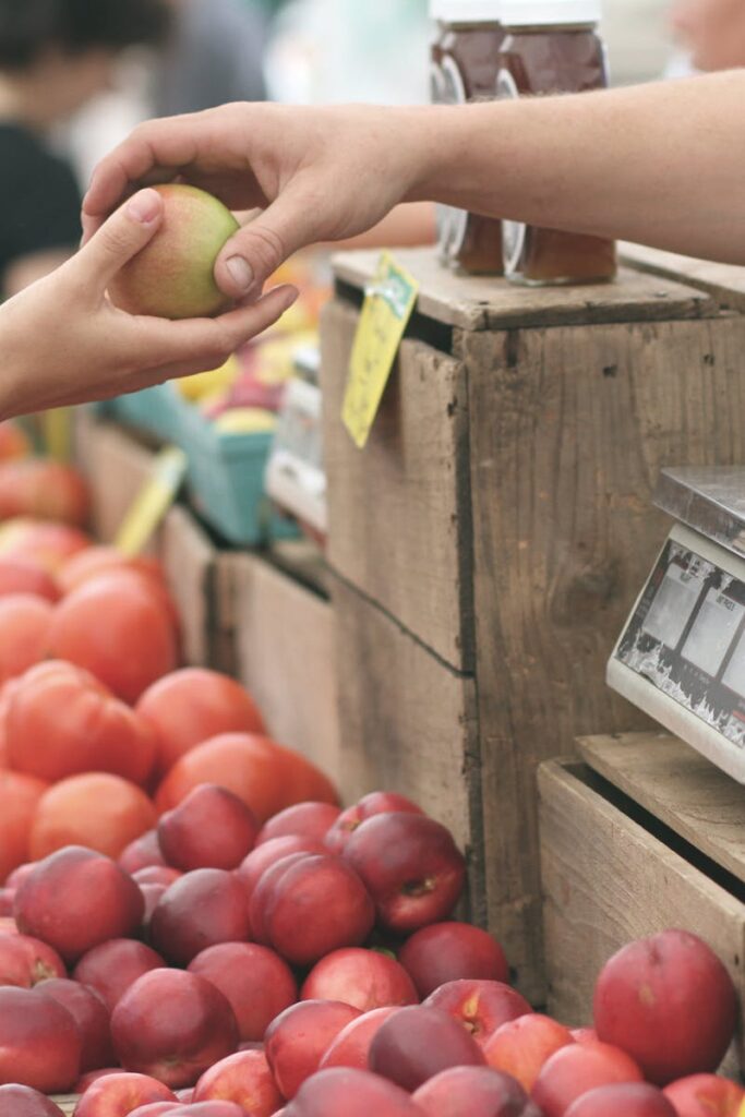 A customer exchanges an apple with a vendor at a vibrant farmers market.